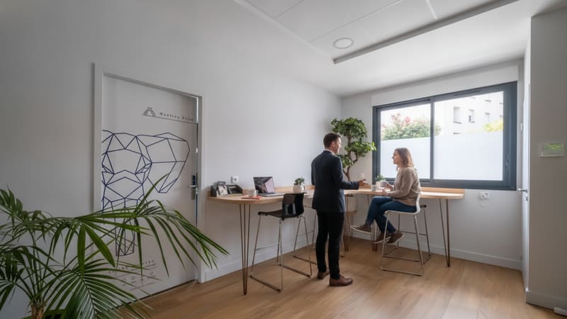 Homme en costume discutant avec une femme assise à un bureau dans un espace de coworking