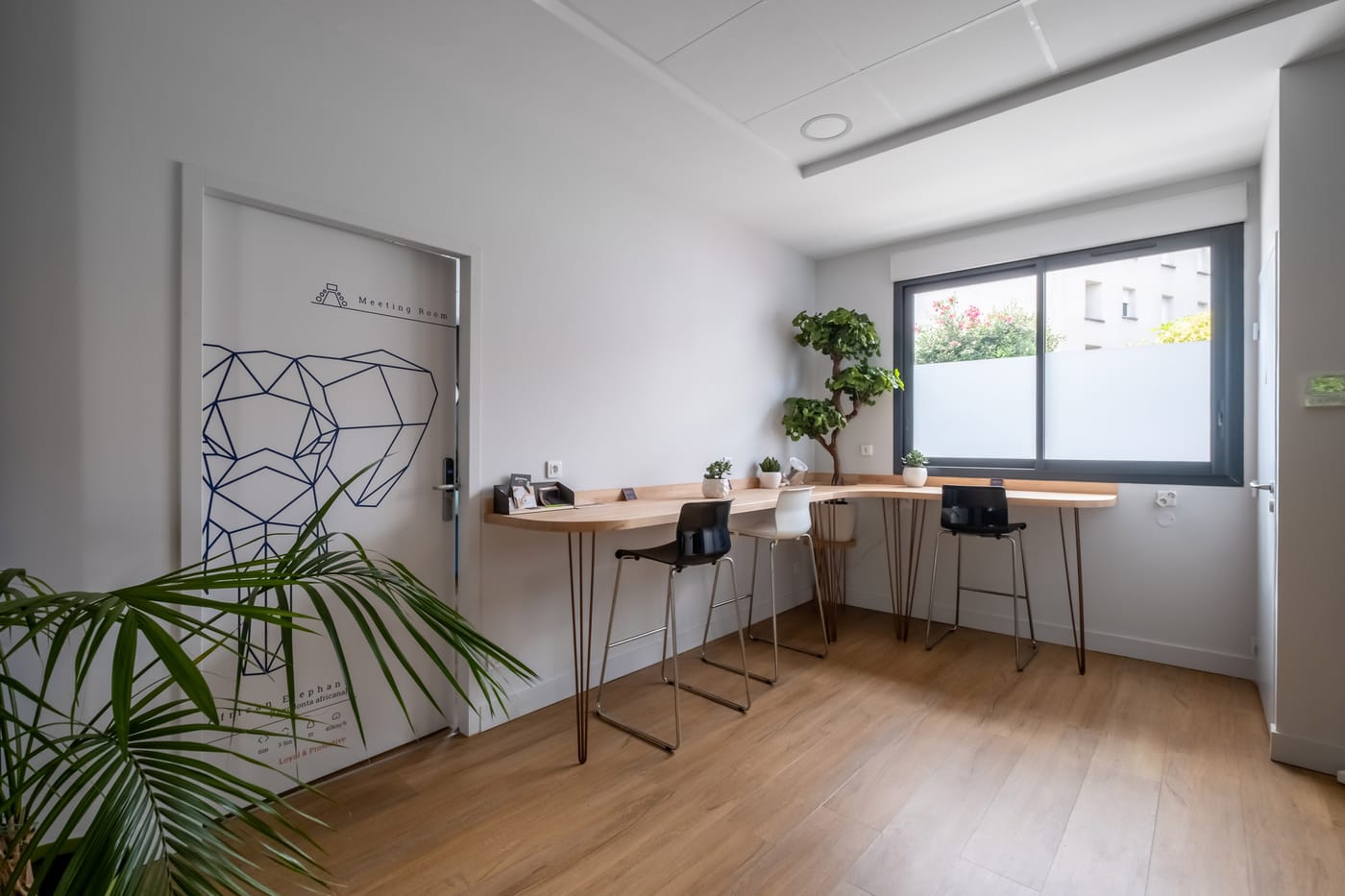 Espace de coworking lumineux avec bureau haut en bois, tabourets et plantes vertes