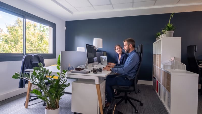 Deux professionnels travaillant sur ordinateur dans un bureau partagé moderne et lumineux