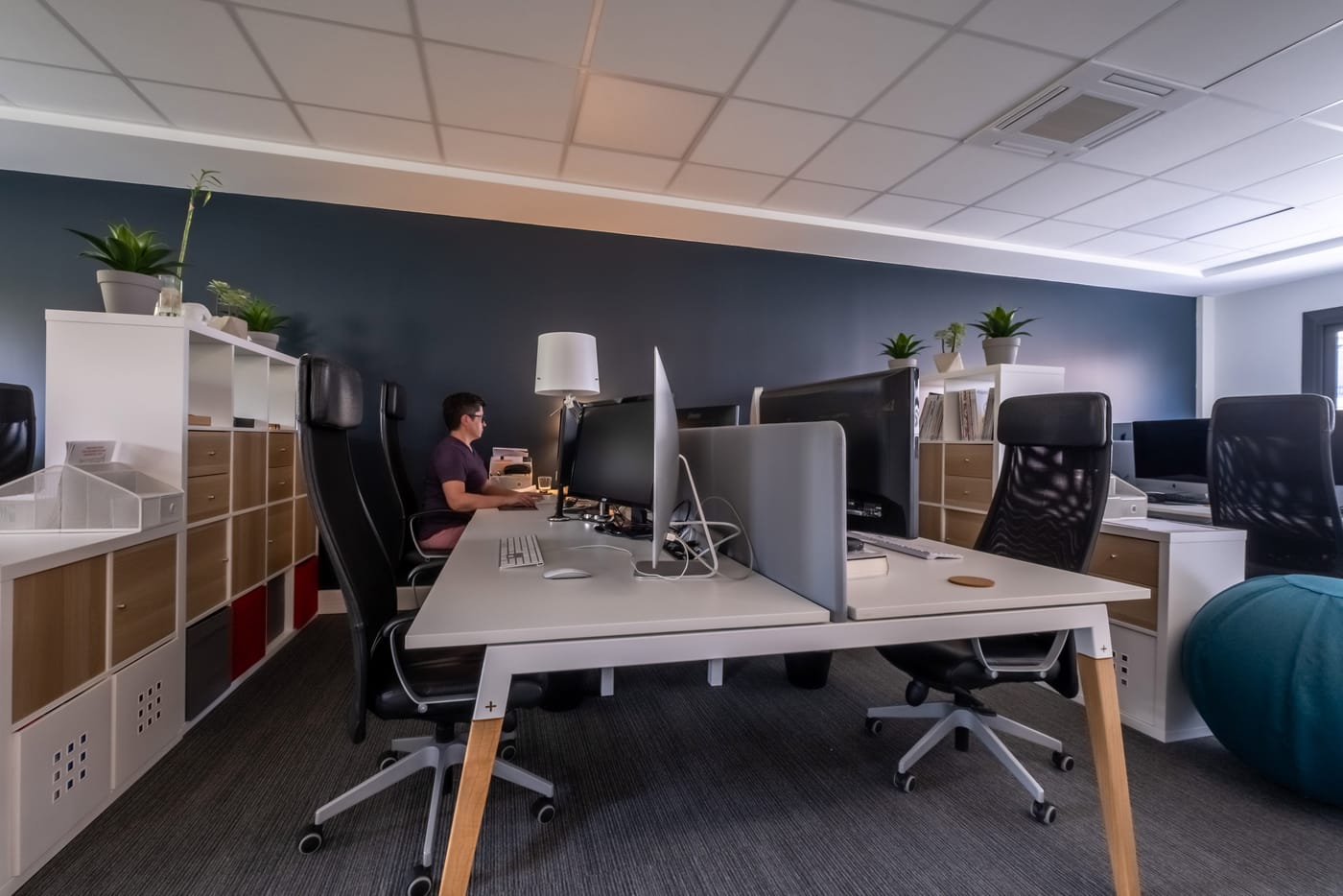 Open space lumineux avec bureaux équipés d'écrans, fauteuils ergonomiques et rangements