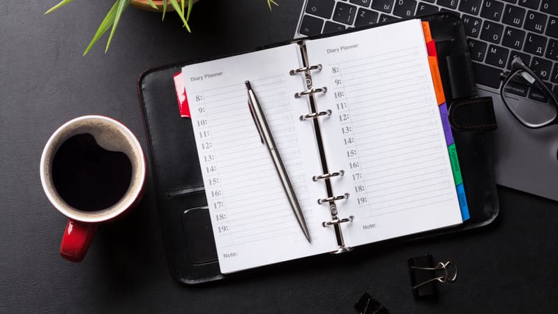 Agenda ouvert avec stylo, tasse de café et ordinateur portable sur un bureau sombre