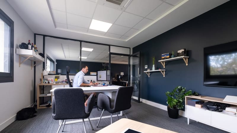 Un homme travaillant sur ordinateur dans un bureau privé chaleureux avec mur bleu et cloison vitrée