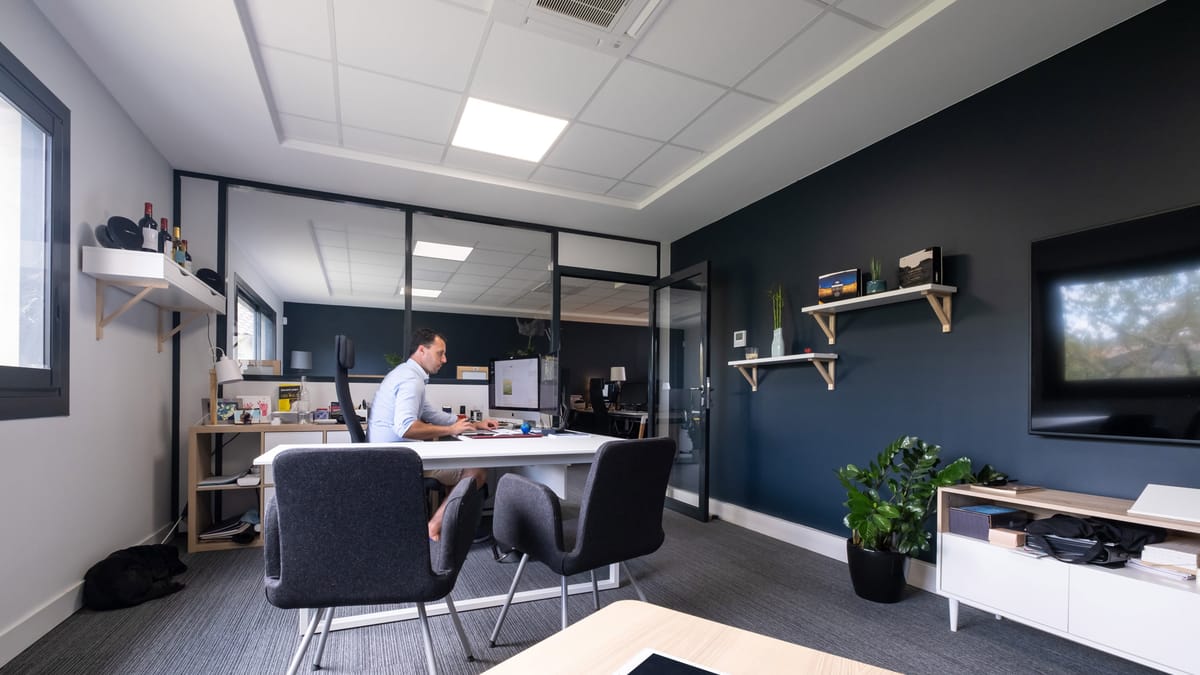 Un homme travaillant sur ordinateur dans un bureau privé chaleureux avec mur bleu et cloison vitrée