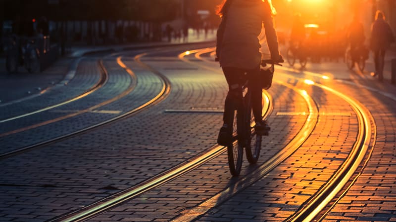 Cycliste circulant à vélo le long des rails de tramway sur une rue pavée au coucher du soleil