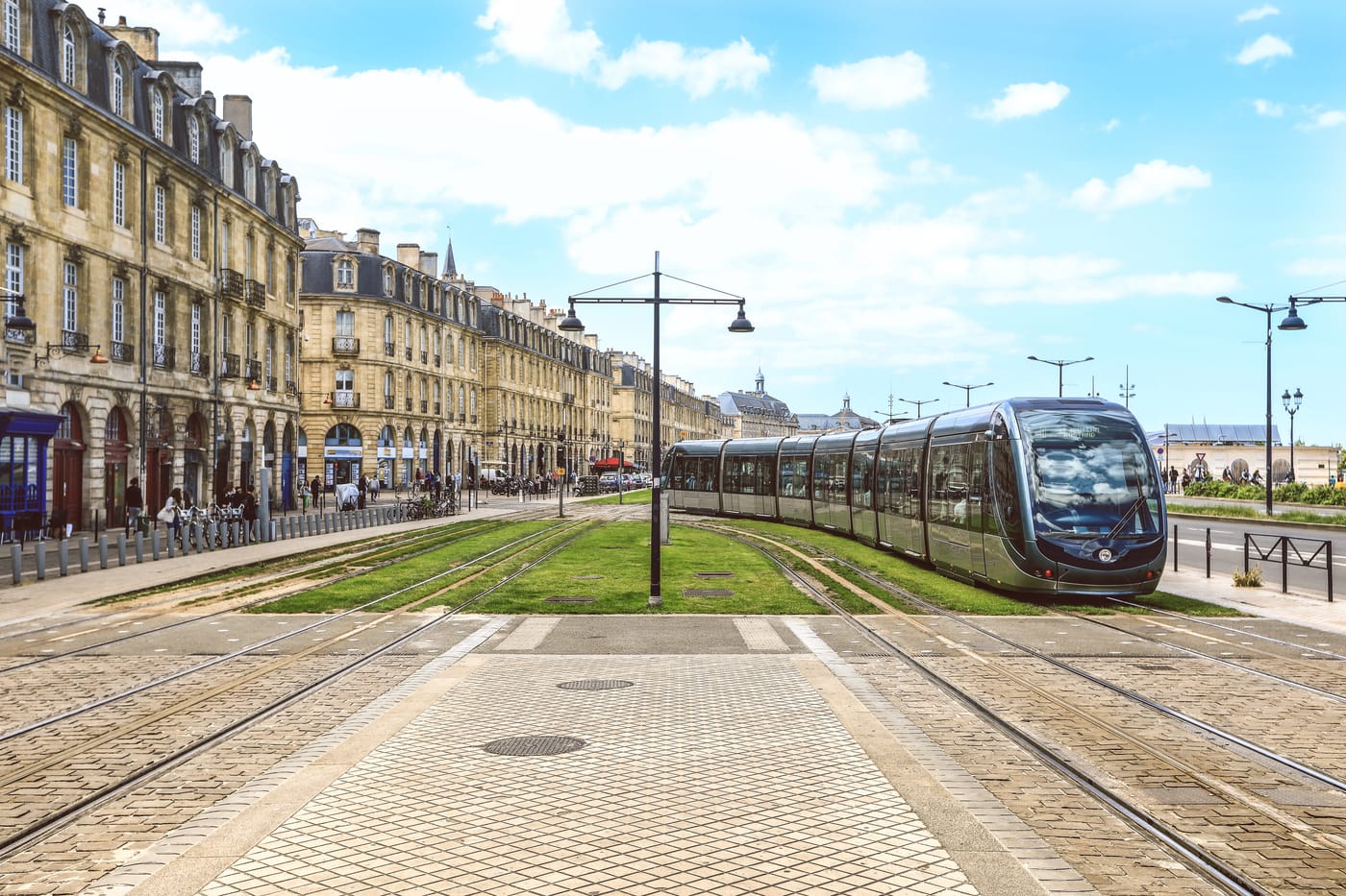 Tramway circulant sur une voie engazonnée devant les immeubles en pierre des quais de Bordeaux