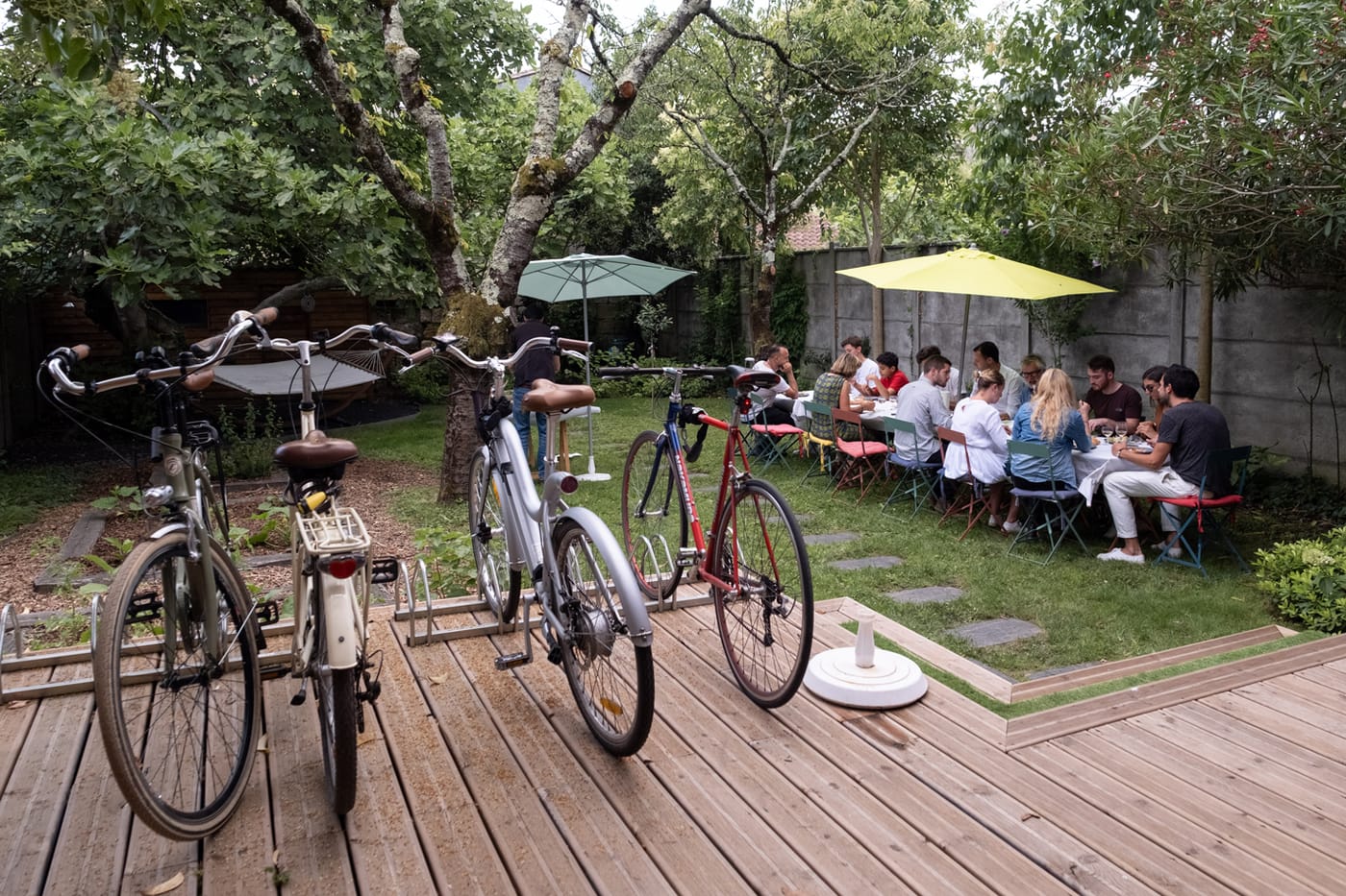 Vélos stationnés sur une terrasse en bois devant un groupe déjeunant dans le jardin